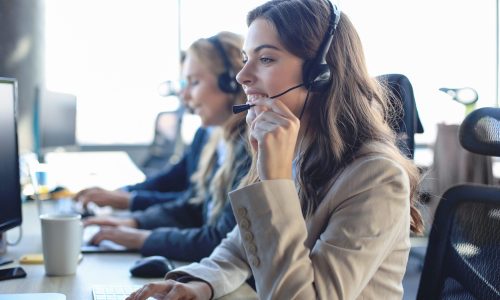 Female customer support operator with headset and smiling, with collegues at background